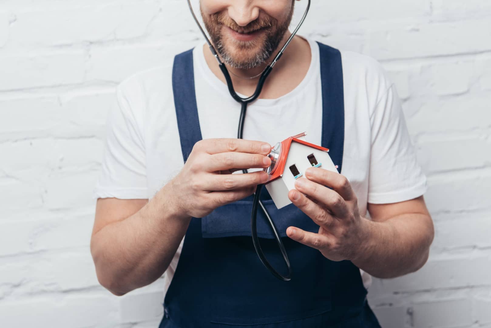 man listening to toy house with stethoscope